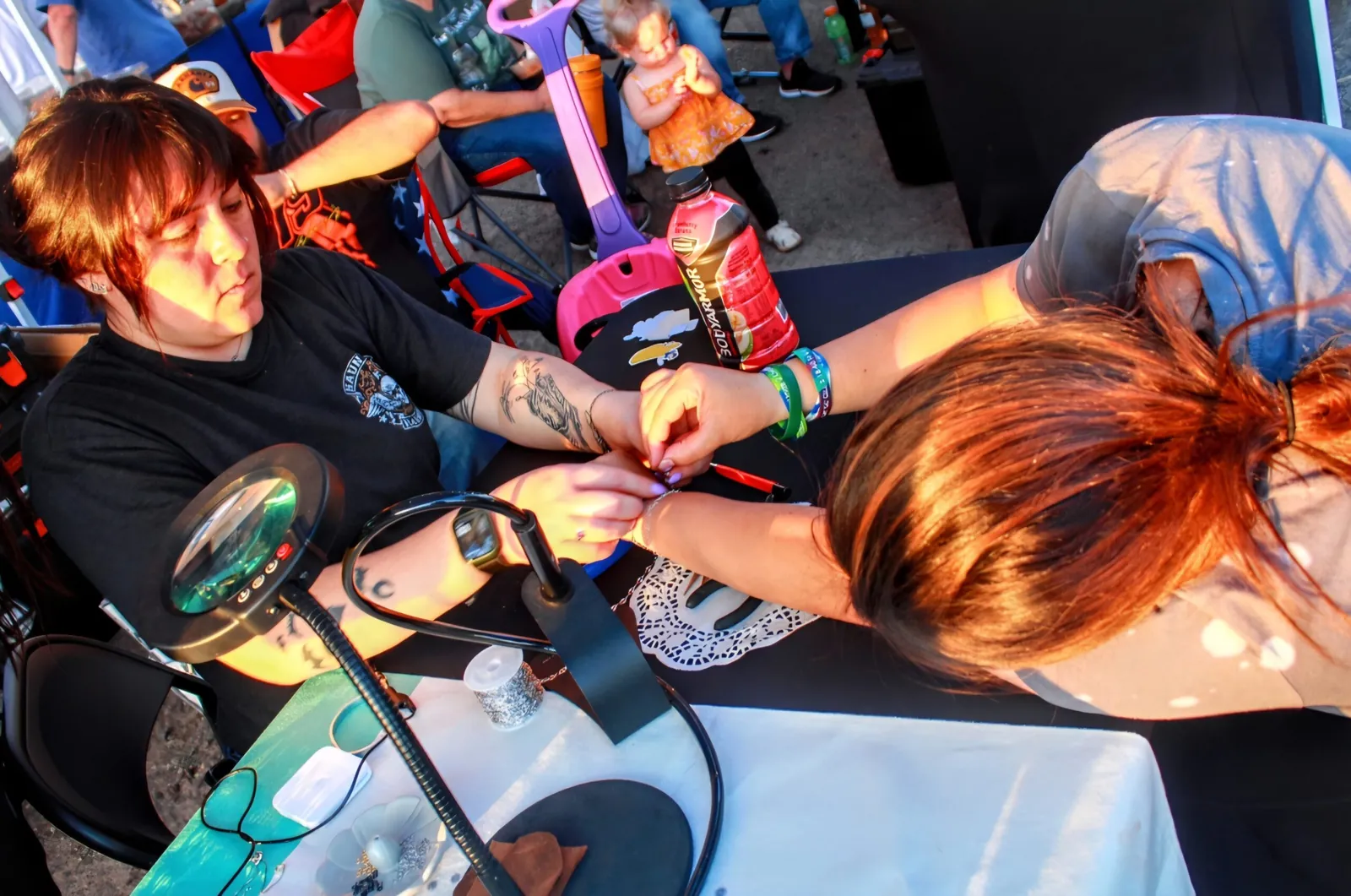 A maker helping a visitor build a custom bracelet at a Buckeye Night Market craft booth